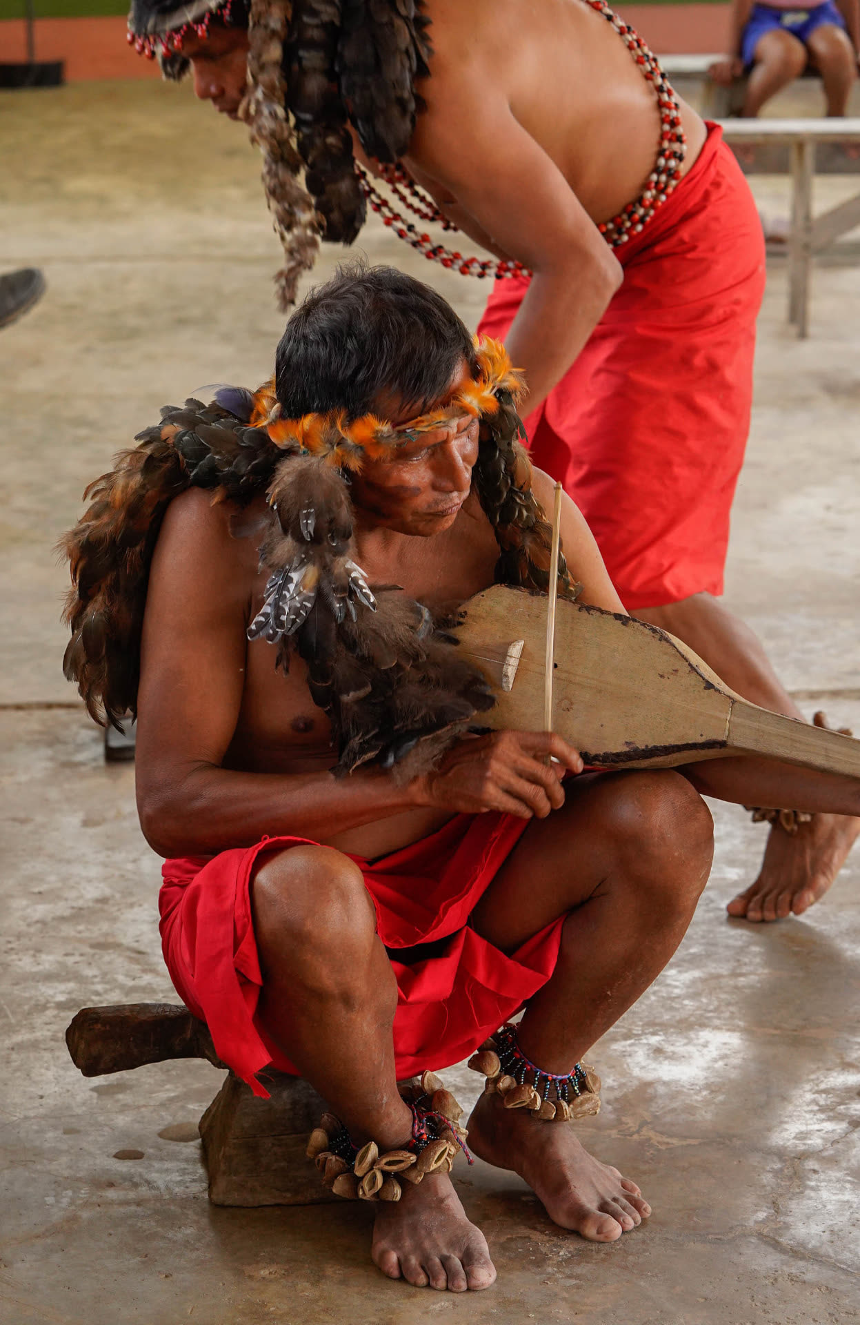 An Awajún elder in a feather headdress playing a traditional bowed instrument