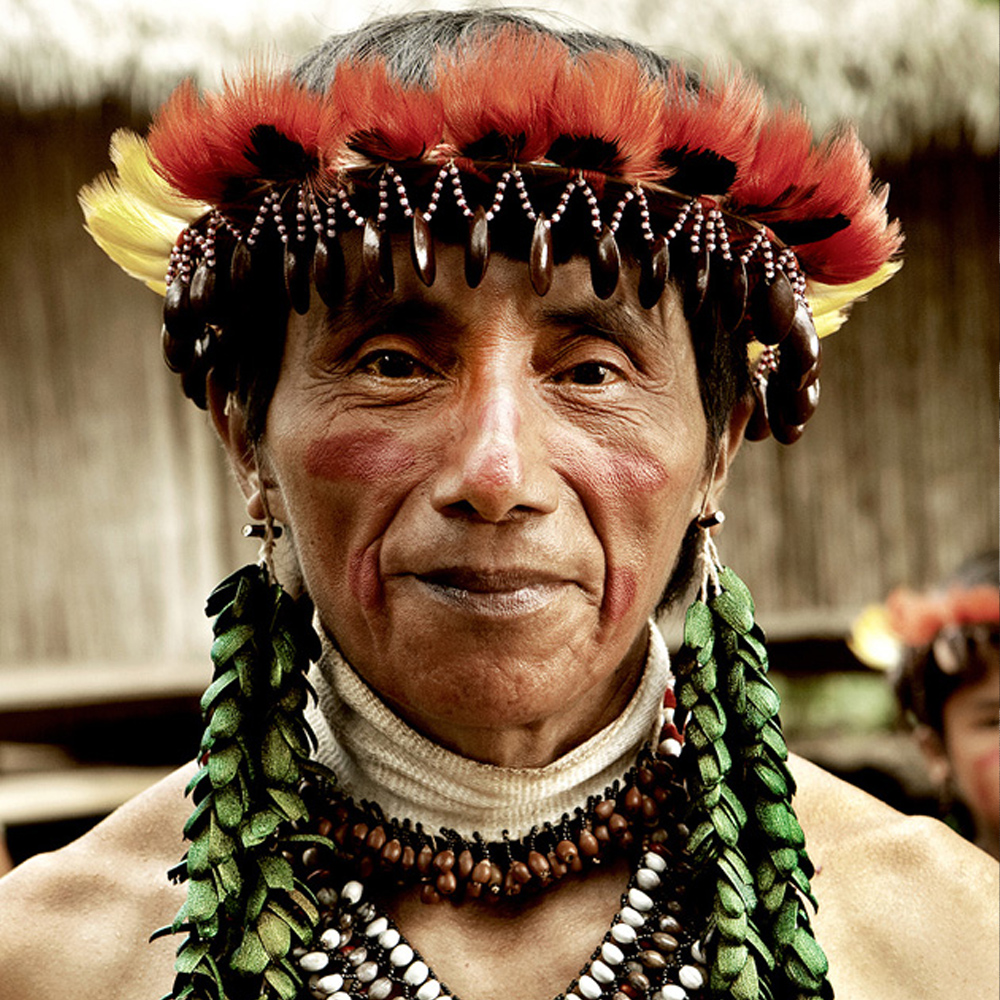 An Awajún man in a feather crown and facial paint, wearing beetle-wing earrings and seed necklaces